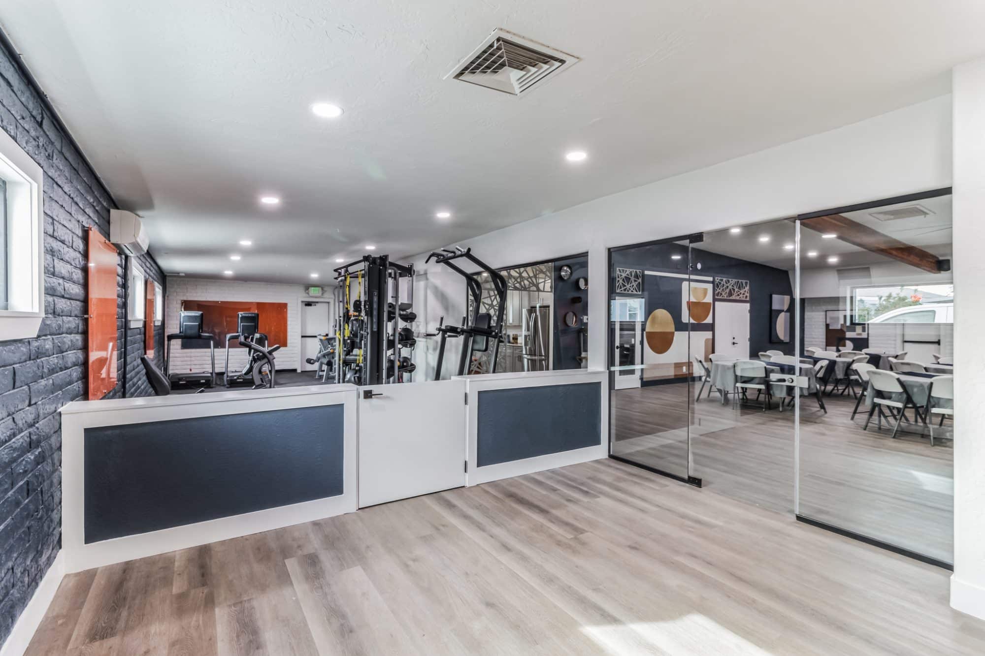 Modern fitness center with treadmills, weight machines, and cardio equipment, separated from a clubhouse lounge by a glass wall and partial partition peoria az