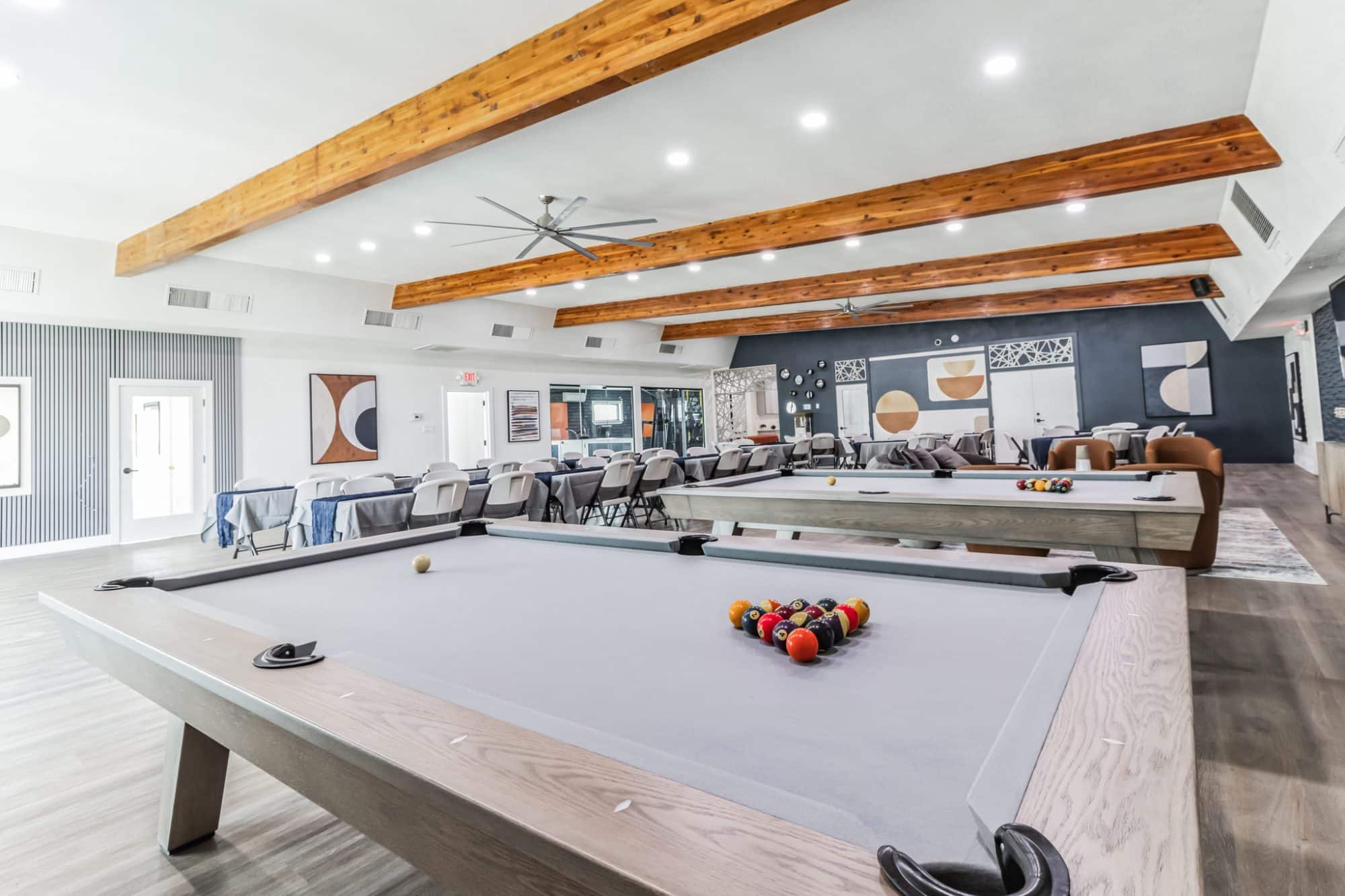Spacious clubhouse featuring two pool tables, dining tables with gray and navy decor, and exposed wooden beams, creating a stylish and social atmosphere peoria az