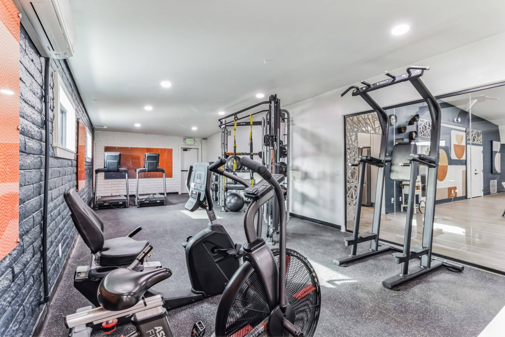 Modern gym with treadmills, weight machines, and stationary bikes, featuring black flooring, mirrored walls, and an orange accent panel peoria az