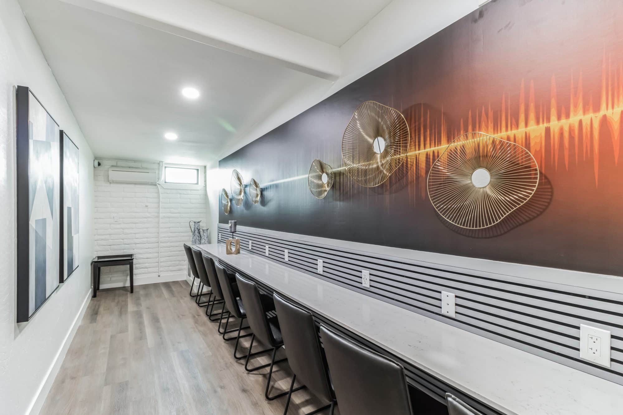 Contemporary co-working space with a long white counter, black chairs, and gold geometric wall art resembling a soundwave, with multiple power outlets peoria az