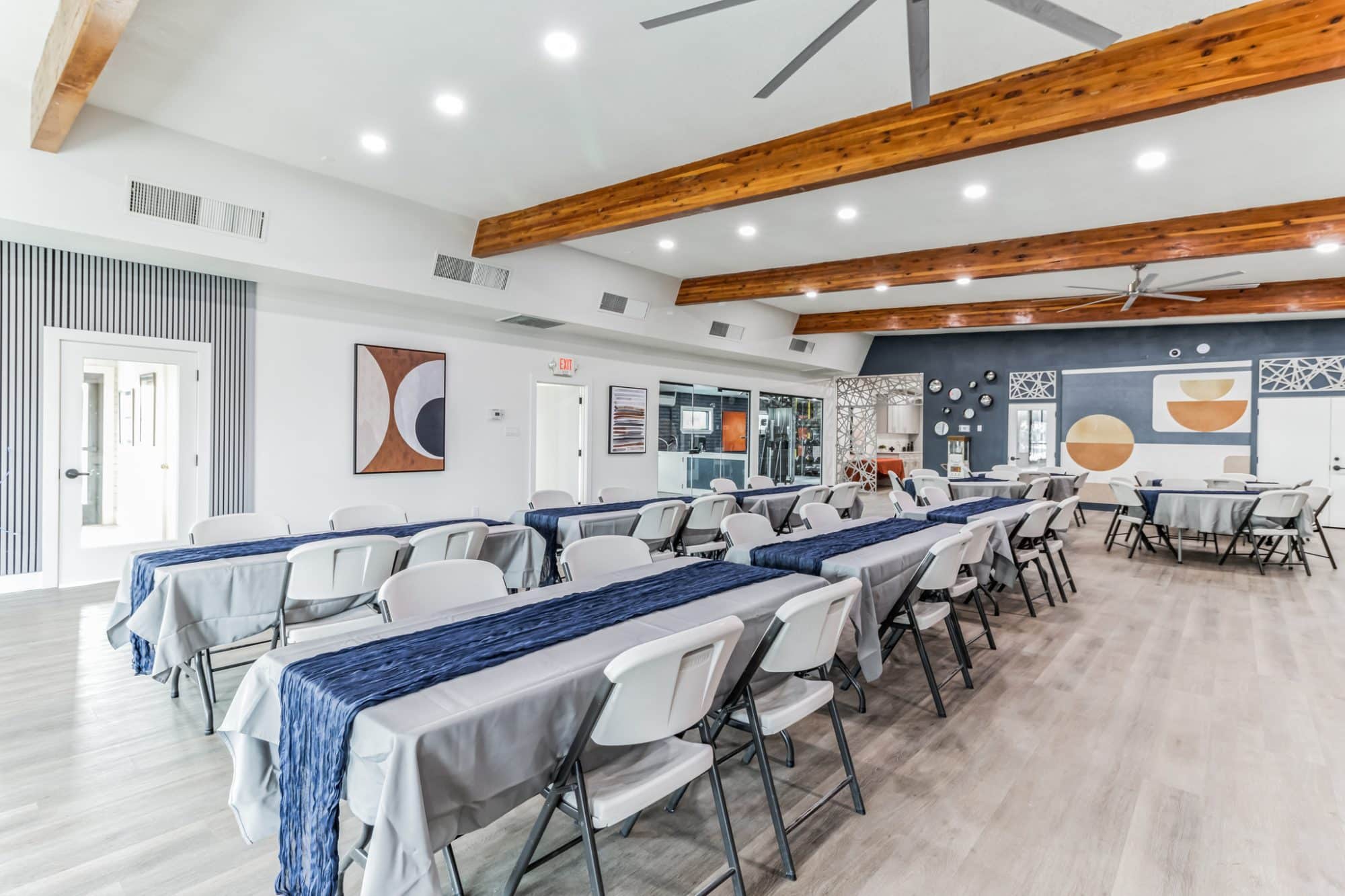 Spacious event hall with long tables covered in gray and navy tablecloths, surrounded by white folding chairs, featuring exposed wooden beams and modern artwork peoria az